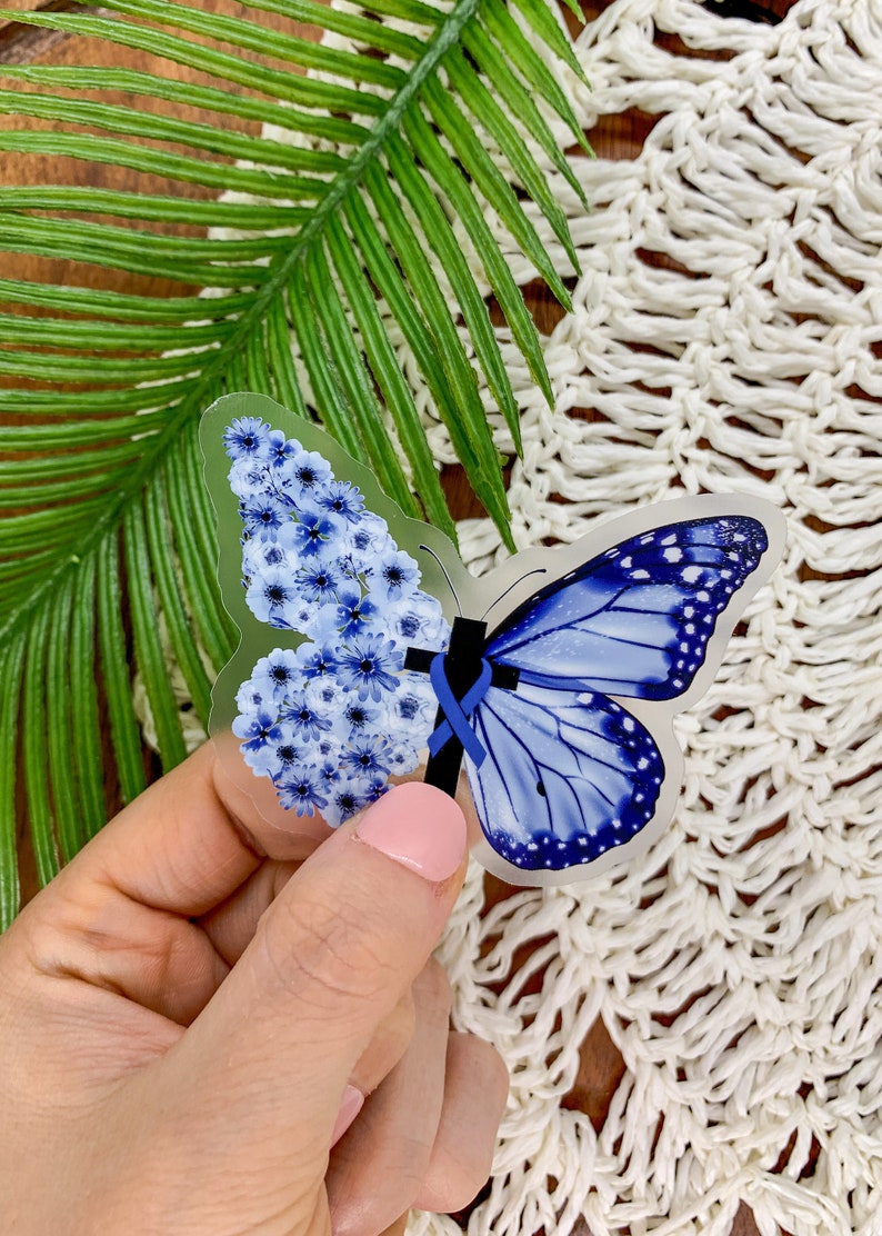 May include: A clear sticker with a blue butterfly design. The butterfly is made of blue flowers on one side and a blue butterfly with white spots on the other side. A blue ribbon is tied around the center of the butterfly.