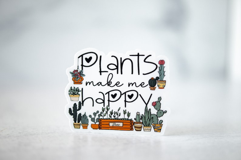 May include: White sticker with the text "Plants make me happy" in black cursive font. The sticker features a variety of potted plants, including cacti, succulents, and leafy plants, all drawn in a cartoon style.