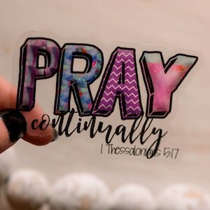 May include: A clear sticker with the word "PRAY" in colorful, patterned letters. The text "continually 1 Thessalonians 5:17" is printed below the word "PRAY".