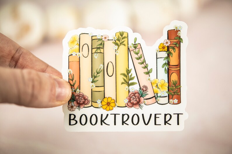 Pu&ograve; includere: Un adesivo con una pila di libri colorati con accenti floreali e il testo "BOOKTROVERT" sotto.