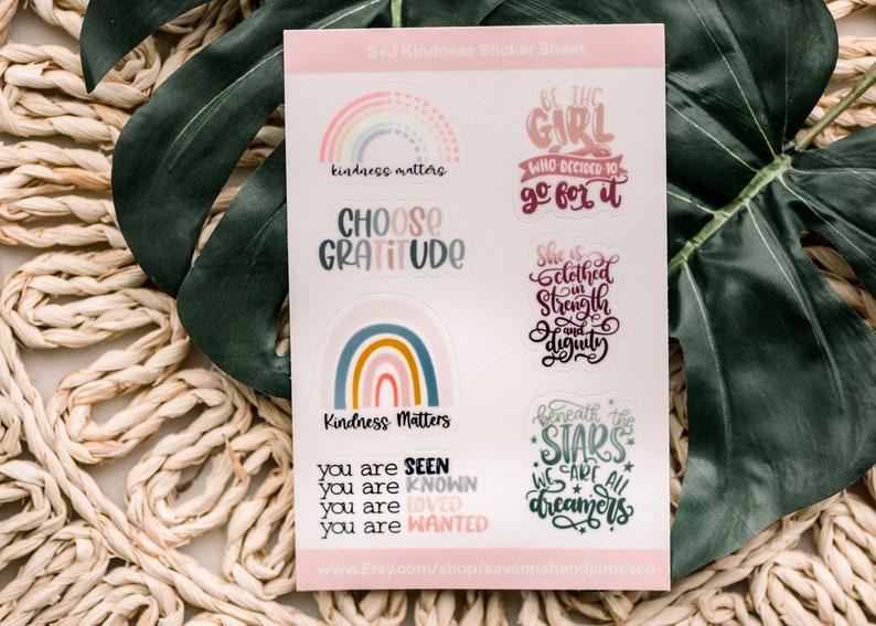 May include: A sheet of stickers with a rainbow theme. The stickers feature positive messages like "kindness matters", "choose gratitude", "be the girl who decided to go for it", "she is clothed in strength and dignity", and "beneath the stars we are all dreamers".