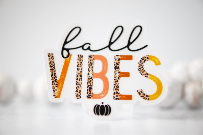 K&ouml;nnte beinhalten: Aufkleber "Fall Vibes" mit Leopardenmuster in Orange, Gelb und Schwarz. Der Aufkleber zeigt den Text "fall vibes" mit einer kleinen K&uuml;rbisgrafik darunter.