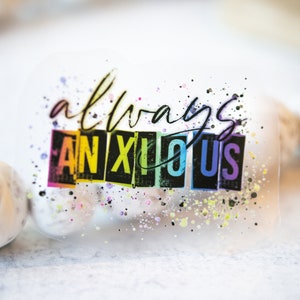 May include: A clear sticker with the words "always anxious" in a handwritten font and block letters. The word "anxious" is in rainbow colors. The sticker has colorful paint splatters around the text.