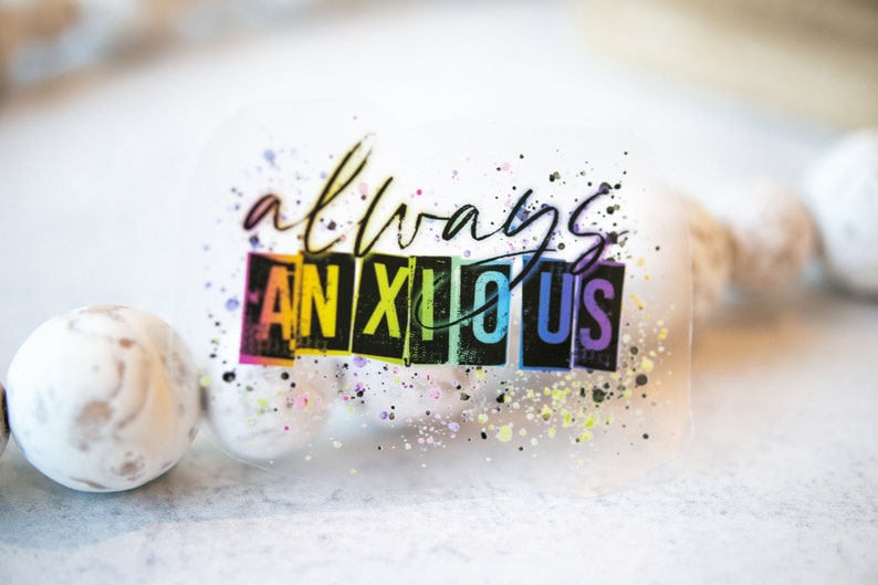 May include: A clear sticker with the words "always anxious" in a handwritten font and block letters. The word "anxious" is in rainbow colors. The sticker has colorful paint splatters around the text.
