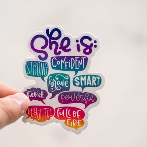 Puede incluir: Una pegatina con el texto "She is: Confident, Strong, Brave, Smart, Fierce, Powerful, Beautiful, Full of Fire" en un degradado arco&iacute;ris.