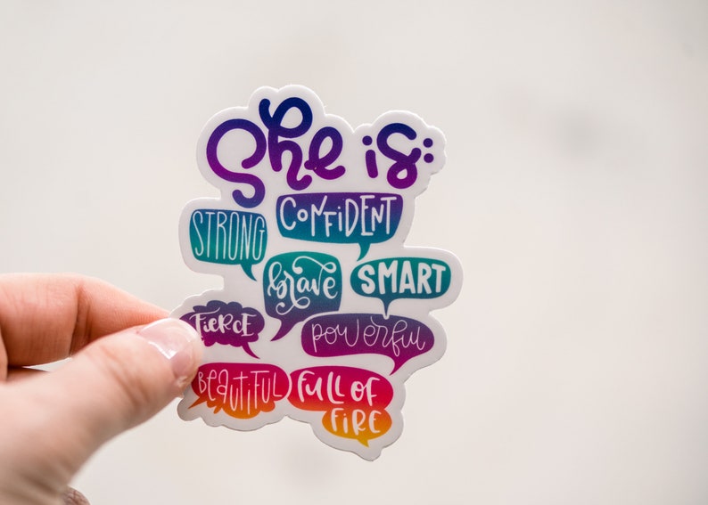 Puede incluir: Una pegatina con el texto "She is: Confident, Strong, Brave, Smart, Fierce, Powerful, Beautiful, Full of Fire" en un degradado arco&iacute;ris.