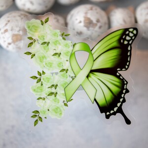 May include: A green butterfly with a green ribbon and white flowers. The butterfly has black markings on its wings.