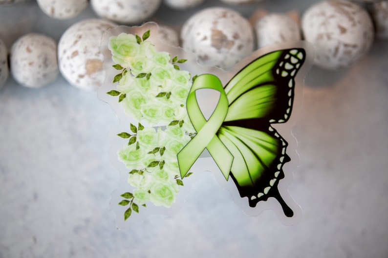 May include: A green butterfly with a green ribbon and white flowers. The butterfly has black markings on its wings.