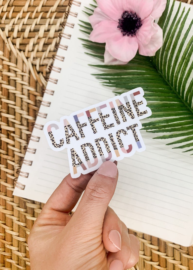 May include: A sticker with the words "CAFFEINE ADDICT" in a leopard print pattern. The sticker is on a white background with a light pink, light blue, and light brown border.