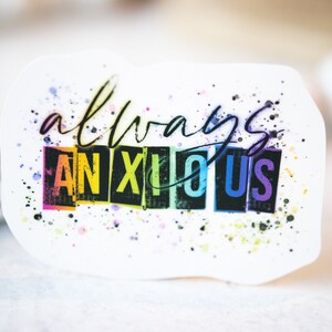 May include: A white sticker with the words "always anxious" in a handwritten style. The word "anxious" is in a rainbow-colored block font. The sticker has colorful paint splatters.
