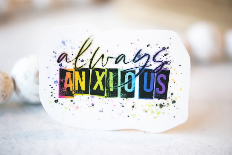 May include: A white sticker with the words "always anxious" in a handwritten style. The word "anxious" is in a rainbow-colored block font. The sticker has colorful paint splatters.