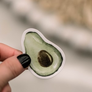 May include: A white sticker with a green avocado illustration. The avocado is cut in half and the pit is visible.