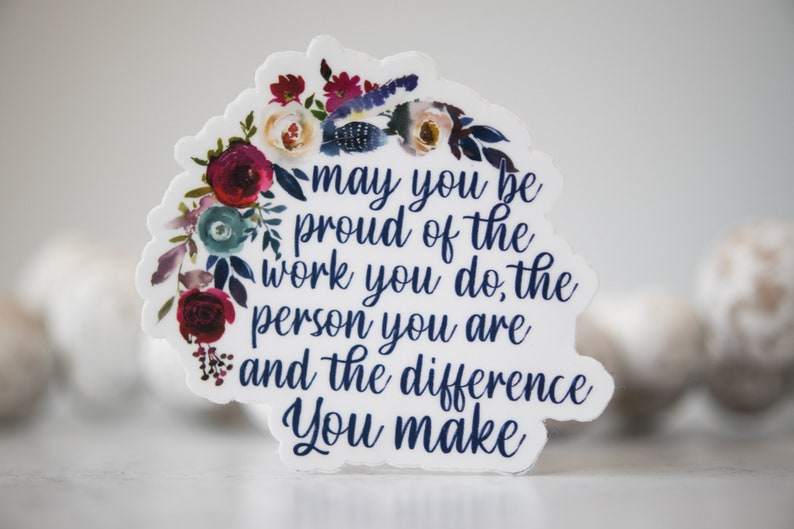 May include: A white sticker with a floral wreath design and the text "may you be proud of the work you do, the person you are and the difference you make".