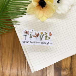 May include: A white sticker with a line of colorful flowers and the text "Grow Positive Thoughts".