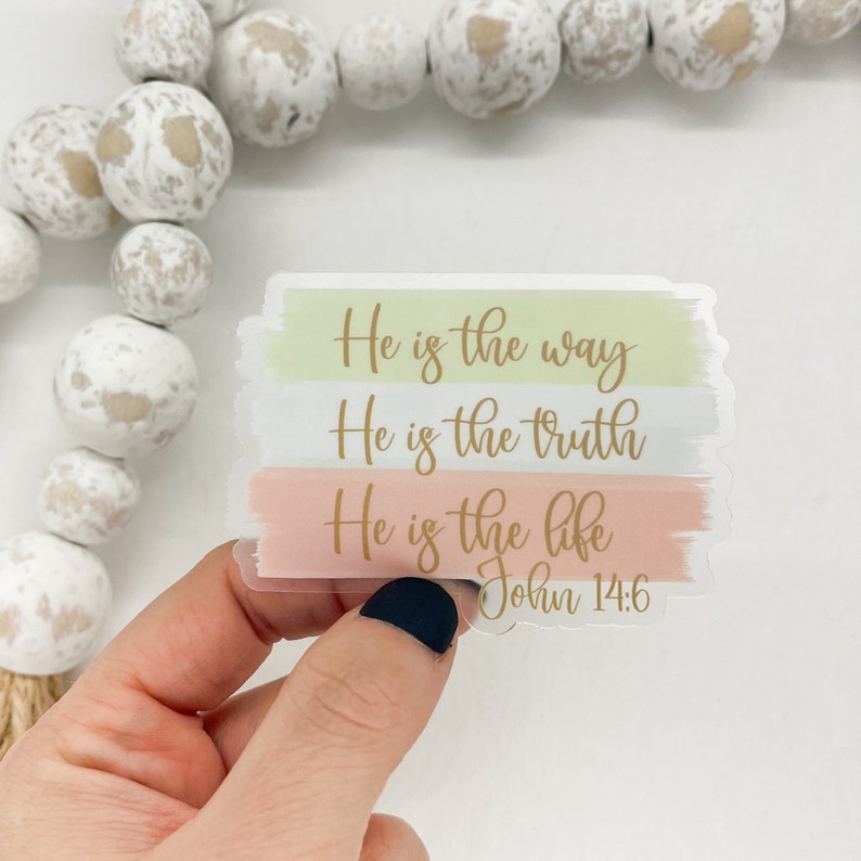 Pode incluir: Um adesivo com fundo de aquarela em tons de verde, azul e rosa. O adesivo apresenta o texto "He is the way, He is the truth, He is the life" em letras douradas. O texto "John 14:6" tamb&eacute;m est&aacute; inclu&iacute;do em letras douradas.