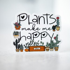 May include: A white sticker with the text "Plants make me happy" in black script. The sticker is decorated with a variety of potted plants, including cacti, succulents, and leafy plants.