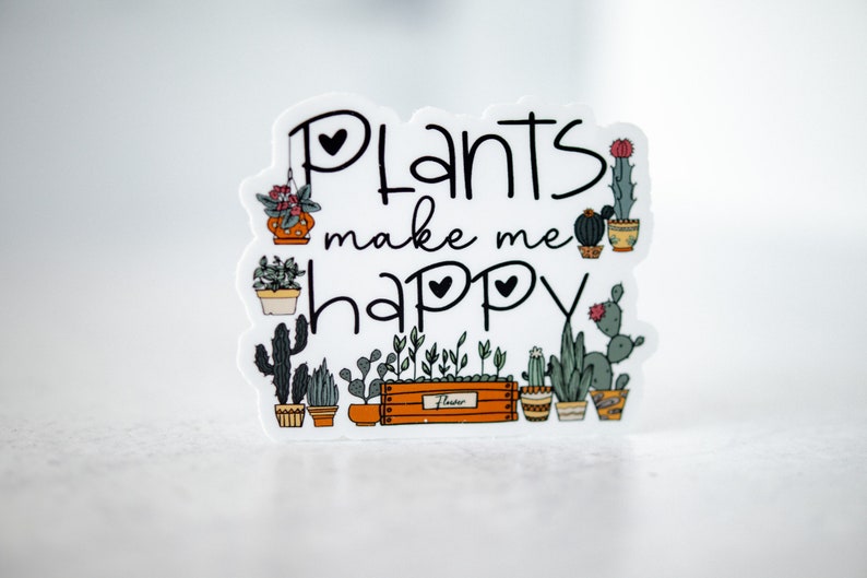May include: A white sticker with the text "Plants make me happy" in black script. The sticker is decorated with a variety of potted plants, including cacti, succulents, and leafy plants.