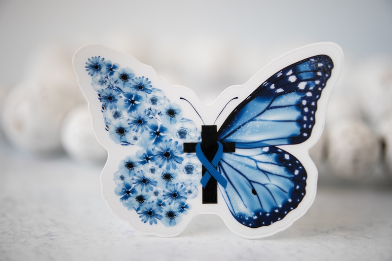 May include: A blue butterfly sticker with a blue ribbon and a black cross. The butterfly is made up of blue flowers on one side and blue wings on the other.
