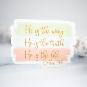 Pode incluir: Um adesivo com fundo de aquarela em tons de rosa e verde. O adesivo apresenta o texto "He is the way, He is the truth, He is the life, John 14:6" em letras douradas.
