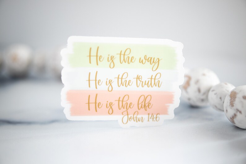 Pode incluir: Um adesivo com fundo de aquarela em tons de rosa e verde. O adesivo apresenta o texto "He is the way, He is the truth, He is the life, John 14:6" em letras douradas.