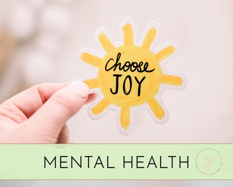 May include: A yellow sun sticker with the text "Choose Joy" written in black. The sticker is being held by a hand.