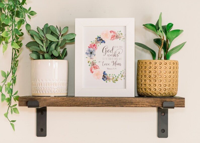 May include: A white framed print with a floral wreath and the text "God works in all things for the good of those who love Him - Romans 8:28"