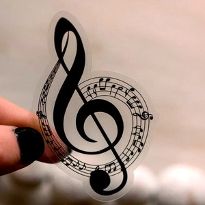 May include: A clear sticker with a black treble clef and musical notes. The sticker is designed to look like a music note.
