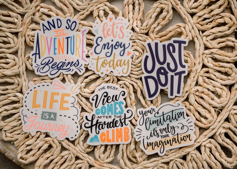 May include: A set of six colorful stickers with motivational quotes. The stickers feature a variety of fonts and colors, including blue, pink, yellow, and green. The quotes include "And so the adventure begins", "Let's enjoy today", "Just do it", "Life is a journey", "The best view comes after the hardest climb", and "Your limitation - it's only your imagination."