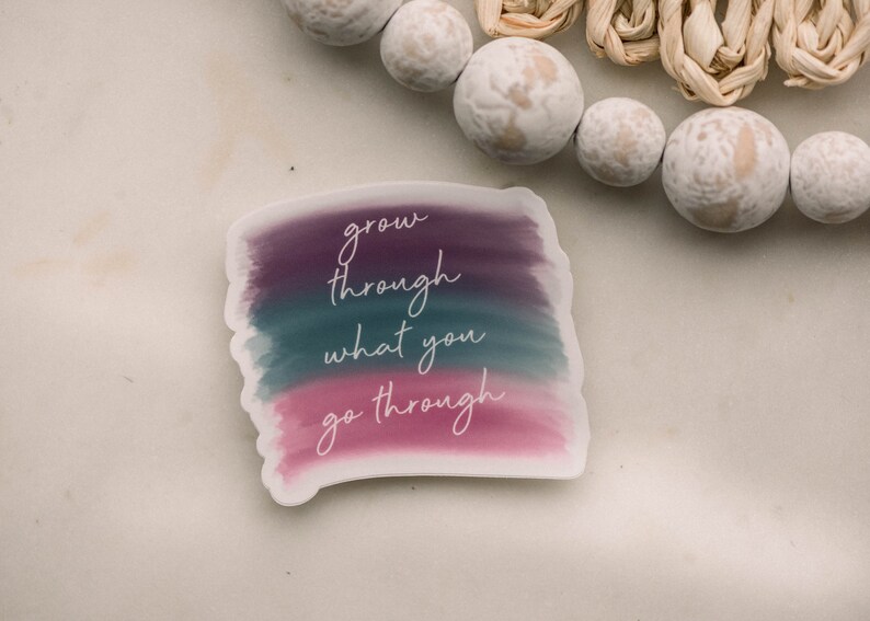 May include: A sticker with a watercolor background in shades of purple, teal, and pink. The sticker has the text "grow through what you go through" written in white cursive.