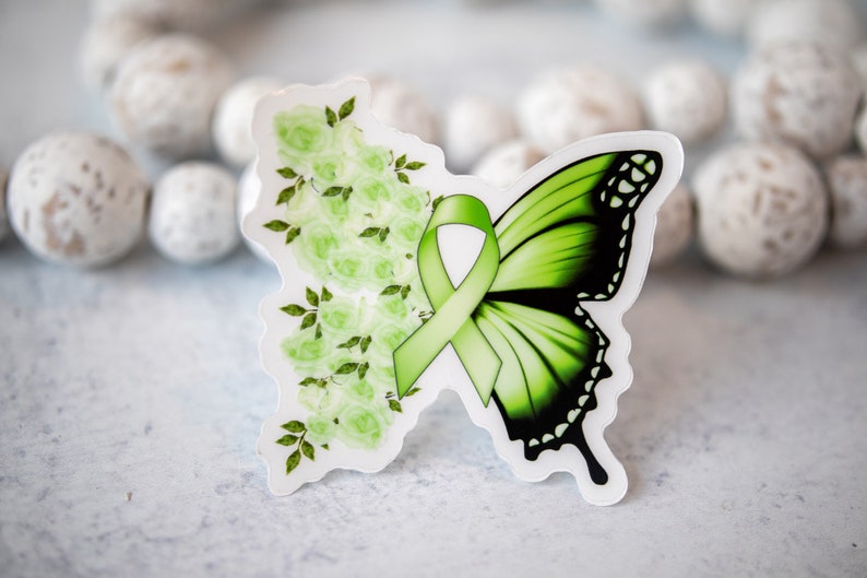 May include: Green butterfly sticker with a green ribbon and white flowers. The butterfly has black markings on its wings.