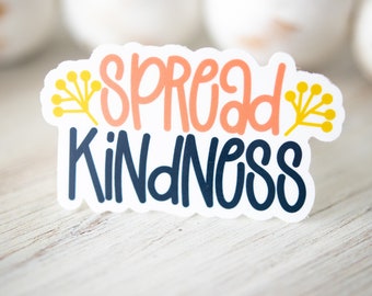 May include: A white sticker with the text "Spread Kindness" in black and orange lettering. The sticker has two yellow floral designs on either side of the text.