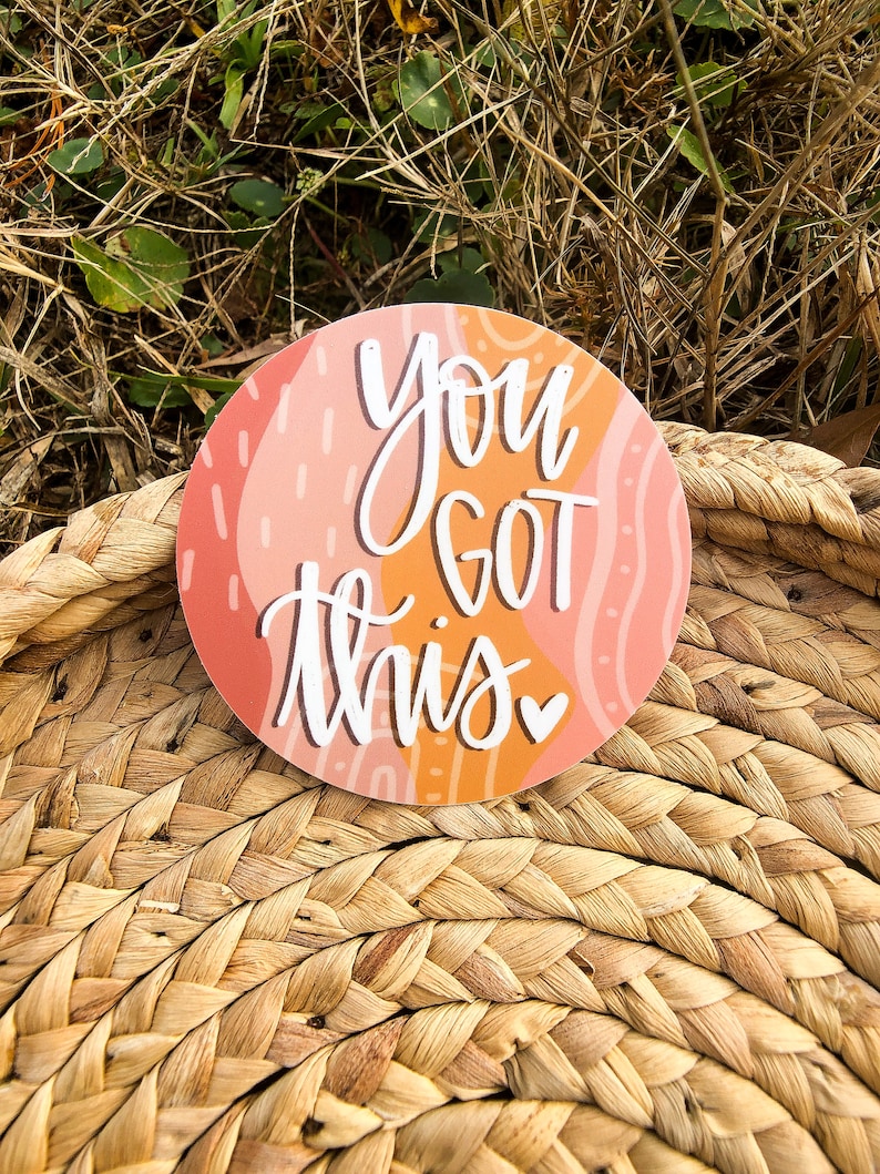 May include: A round sticker with an abstract pink and orange design. The sticker says "You got this" in white cursive lettering with a small heart.