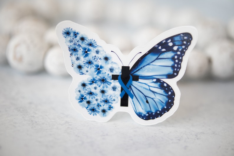 May include: A blue butterfly sticker with a blue ribbon and a black cross on its body. The butterfly is made up of blue flowers on one side and blue wings on the other.