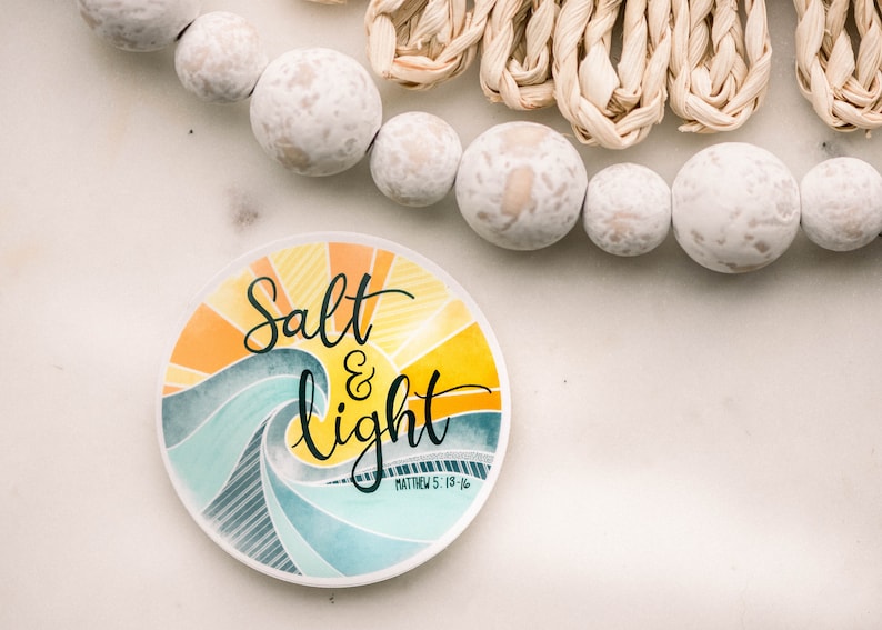 May include: A round sticker with a watercolor design of a sun rising over a wave. The sticker says "Salt & light" with the scripture reference "Matthew 5:13-16" underneath.