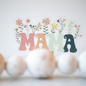 Pode incluir: Um sinal colorido de "MAMA" com flores e folhas. O sinal &eacute; feito de papel e tem um estilo retro e caprichoso.