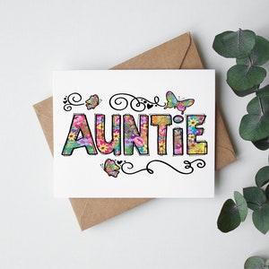 May include: A white card with the word "AUNTIE" spelled out in colorful letters. The letters are decorated with flowers and butterflies. The card is on a brown envelope.