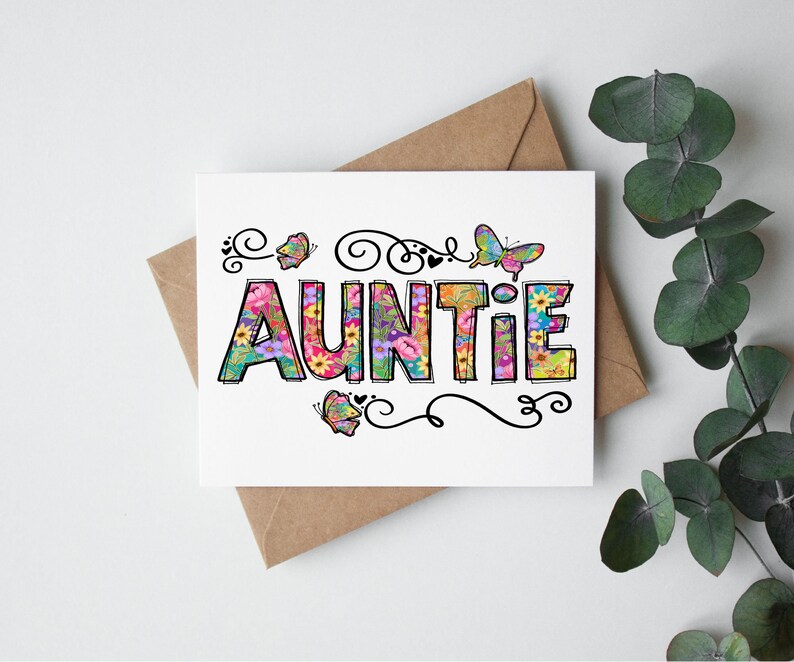 May include: A white card with the word "AUNTIE" spelled out in colorful letters. The letters are decorated with flowers and butterflies. The card is on a brown envelope.