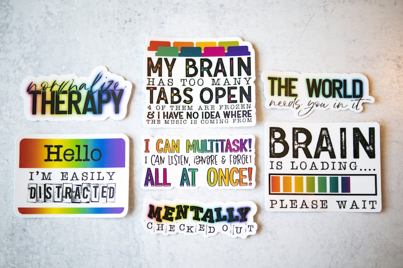 May include: Set of ten colorful stickers with humorous sayings about mental health and multitasking. The stickers feature rainbow colors and black text. The sayings include "Normalize Therapy", "My Brain Has Too Many Tabs Open", "The World Needs You In It", "Hello I'm Easily Distracted", "I Can Multitask! I Can Listen, Ignore & Forget All At Once!", "Mentally Checked Out", "Brain Is Loading... Please Wait".