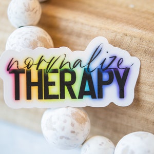 May include: A rainbow-coloured sticker with the text "normalize THERAPY" in black lettering.