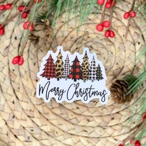 Puede incluir: Una pegatina blanca con una fila de cinco &aacute;rboles de Navidad en diferentes patrones, incluyendo cuadros, estampado de leopardo y vichy. Los &aacute;rboles est&aacute;n delineados en negro y el texto "Merry Christmas" est&aacute; escrito en cursiva negra debajo de los &aacute;rboles.