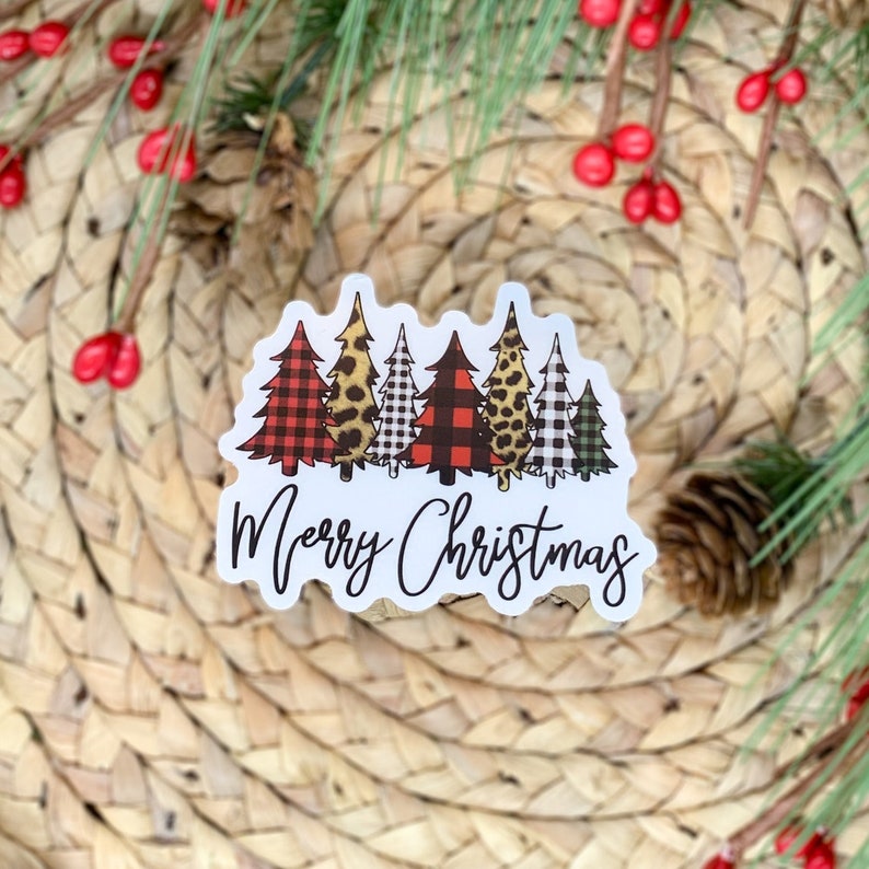 Puede incluir: Una pegatina blanca con una fila de cinco &aacute;rboles de Navidad en diferentes patrones, incluyendo cuadros, estampado de leopardo y vichy. Los &aacute;rboles est&aacute;n delineados en negro y el texto "Merry Christmas" est&aacute; escrito en cursiva negra debajo de los &aacute;rboles.