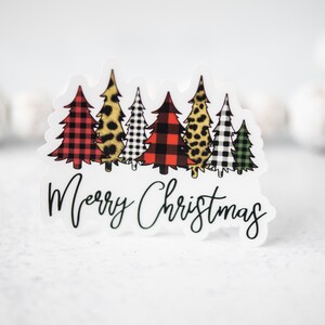 Puede incluir: Una pegatina blanca con una fila de cinco &aacute;rboles de Navidad en diferentes patrones. Los &aacute;rboles son de cuadros rojos y negros, estampado de leopardo, cuadros negros y blancos, cuadros rojos y negros y cuadros verdes y blancos. El texto "Feliz Navidad" est&aacute; escrito en cursiva negra debajo de los &aacute;rboles.