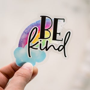 May include: A clear sticker with a rainbow and a cloud. The sticker says "Be kind" in black text.