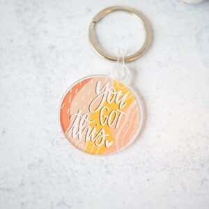 May include: A round, clear acrylic keychain with a colorful abstract design and the text "You Got This" in white lettering.