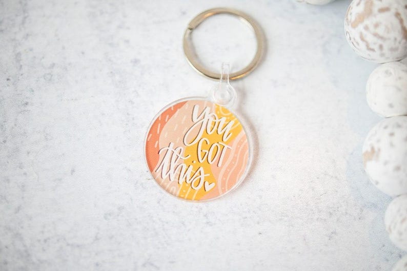 May include: A round, clear acrylic keychain with a colorful abstract design and the text "You Got This" in white lettering.