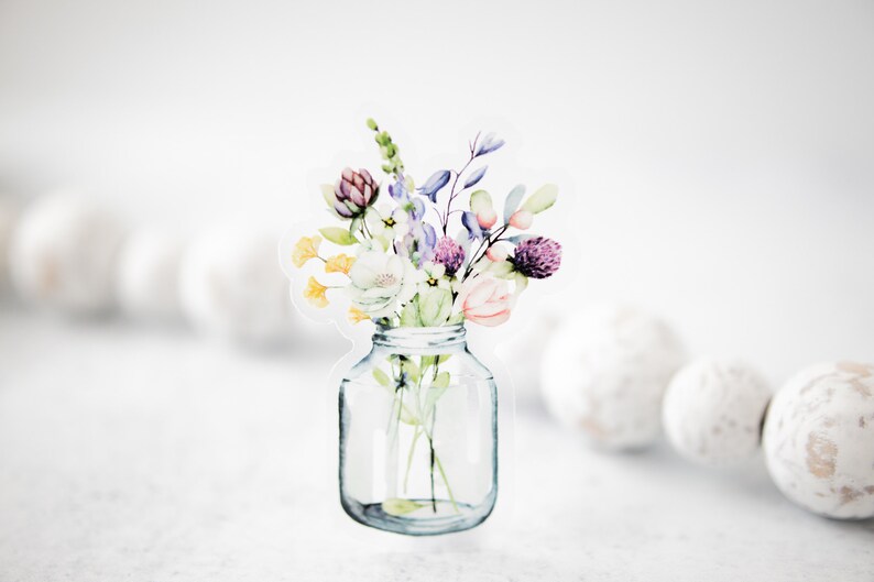 May include: A watercolor illustration of a bouquet of flowers in a clear glass jar. The flowers are in shades of pink, purple, yellow, and green.