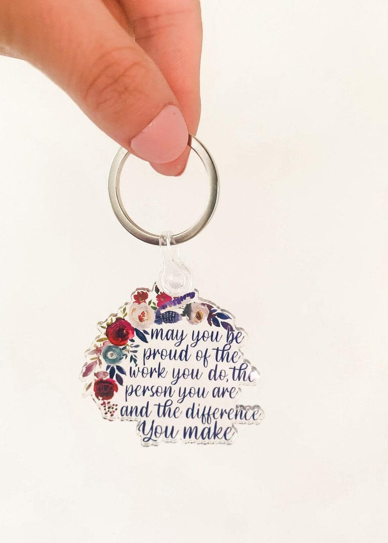 May include: A clear acrylic keychain with a floral design and the text "may you be proud of the work you do, the person you are and the difference you make".