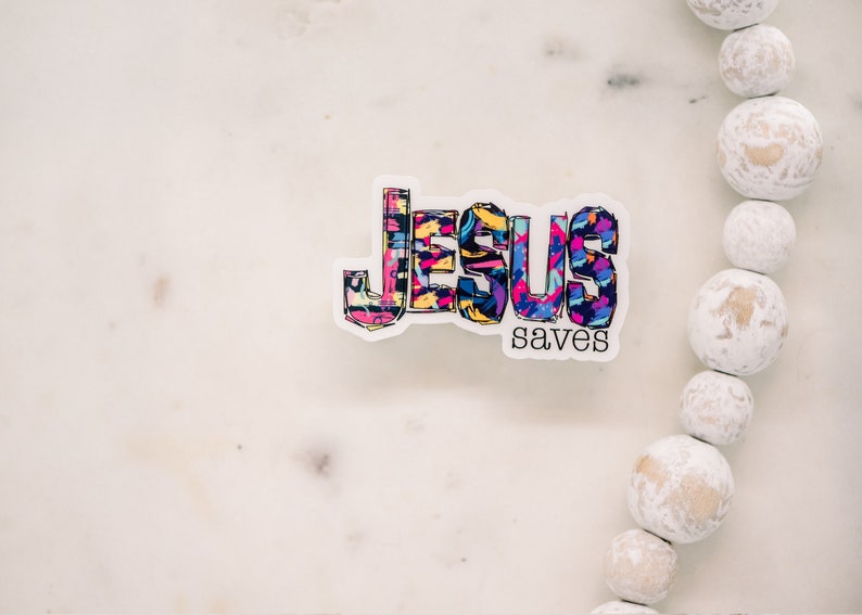 May include: A colorful sticker with the words "Jesus saves" in a bold, graphic font. The letters are filled with a variety of bright colors and patterns.