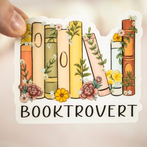 Pu&ograve; includere: Un adesivo con una pila di libri colorati con accenti floreali e il testo "BOOKTROVERT".