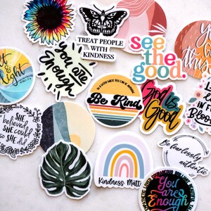 May include: Assortment of colorful stickers with positive messages and designs, including a sunflower, a butterfly, a rainbow, a monstera leaf, and text like "You are enough", "Be Kind", "God is Good", "See the good", and "Live life in full bloom".